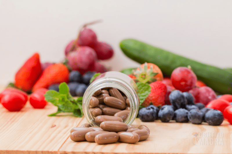 OM Vitta Life | A Empresa Objetivo Magra - Frutas e legumes espalhados sobre a mesa e um pode de cápsulas virado, algumas cápsulas soltas da OM Vitta Life.